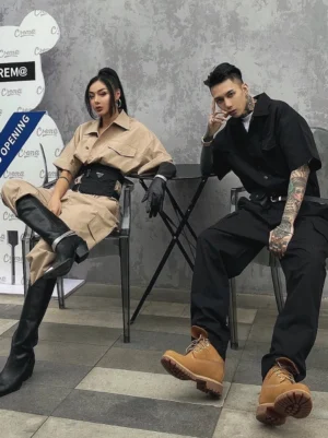 Couples wearing khaki and black utility cargo jumpsuits with wide waist belts and flap pockets in an outdoor streetwear setting