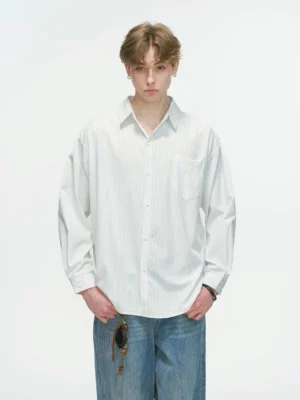 Male model wearing a white vertical stripe relaxed oversized overshirt with chest pocket, wide-leg blue jeans, and sunglasses in a clean studio setting