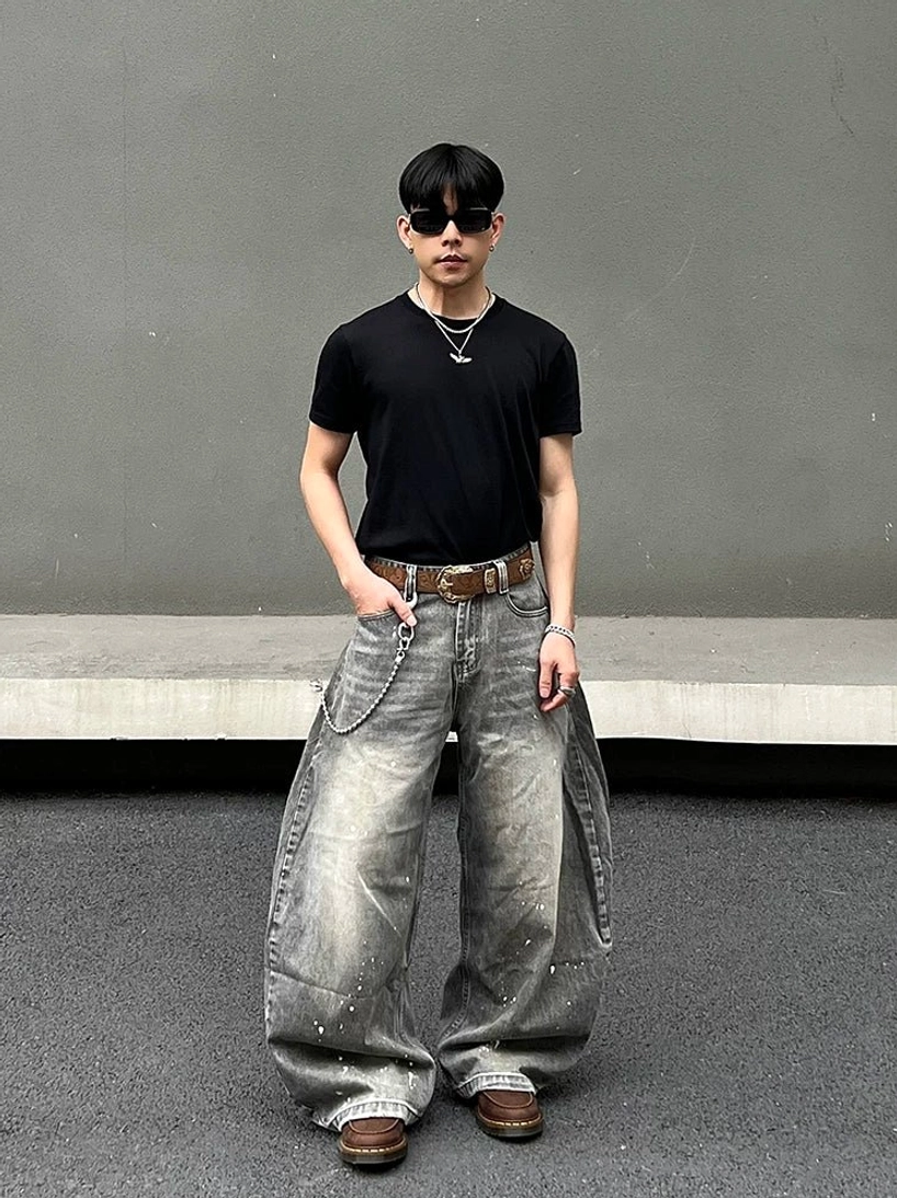 Front view of vintage acid wash balloon jeans with white paint splatters, left thigh cargo pocket, wallet chain, black shirt, sunglasses, and industrial streetwear styling