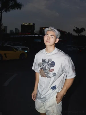 Left three quarter view of an Asian male model wearing an oversized washed off white vintage badge graphic streetwear T-shirt in an urban parking lot