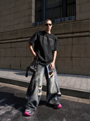 Front view of vintage blue distressed ultra-wide leg denim jeans styled with a black graphic T-shirt and chunky sneakers on an urban street
