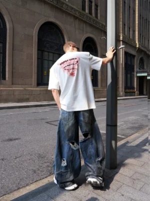 Rear view of faded blue oversized distressed wide-leg jeans with frayed knee rips and an extra baggy streetwear silhouette