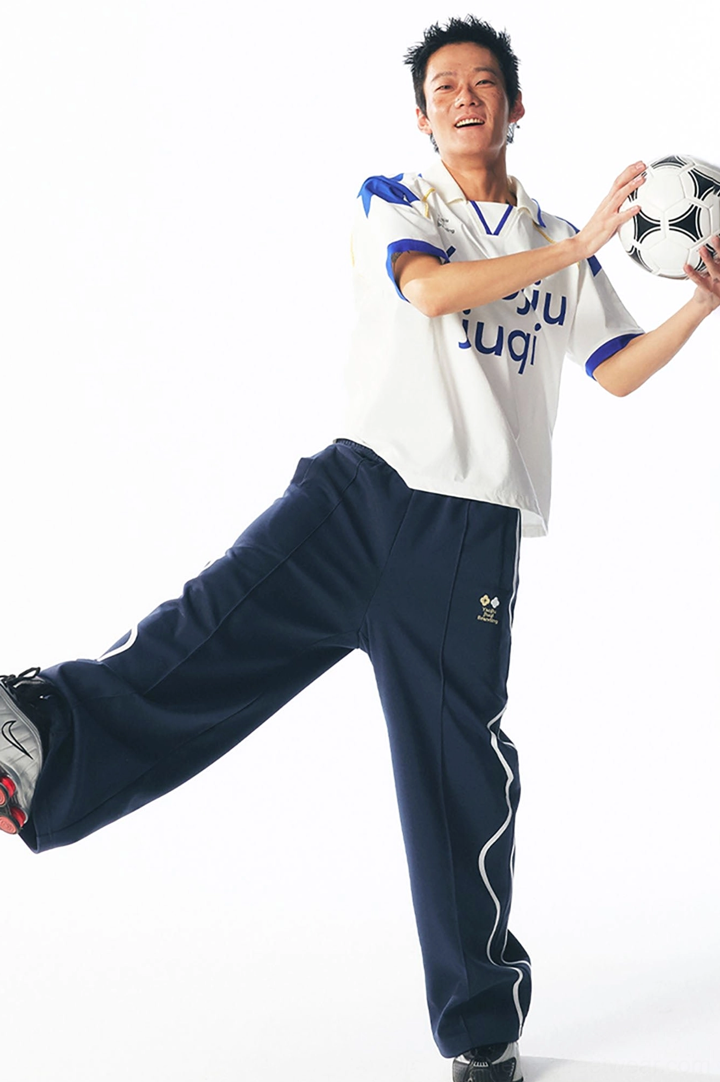 Dynamic vintage sportswear look with a blue and white contrast V-neck football jersey, wide-leg navy pants, and a soccer ball