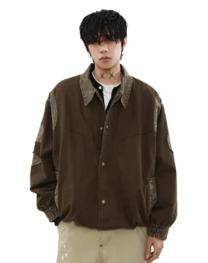 Front view of a male model wearing a vintage dark brown canvas bomber jacket with oversized Korean streetwear fit, metal snap buttons, pointed collar, contrast faded shoulder trim, and khaki trousers