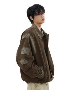 Three-quarter side view of a vintage brown canvas bomber jacket showing hidden hand pockets, embroidered sleeve patches, ribbed cuffs, elasticated hem, and relaxed streetwear silhouette