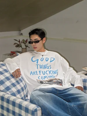 Three-quarter sitting view of white oversized cassette graphic long sleeve streetwear tee styled with wide leg blue jeans
