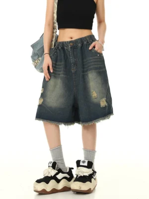 Vintage distressed blue denim Bermuda shorts worn by model in black cropped top, left front three-quarter streetwear view