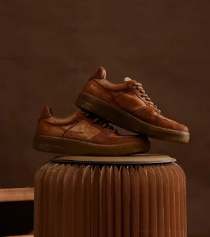 Brown distressed leather casual sneakers with tonal laces and vintage textured upper on dark studio background