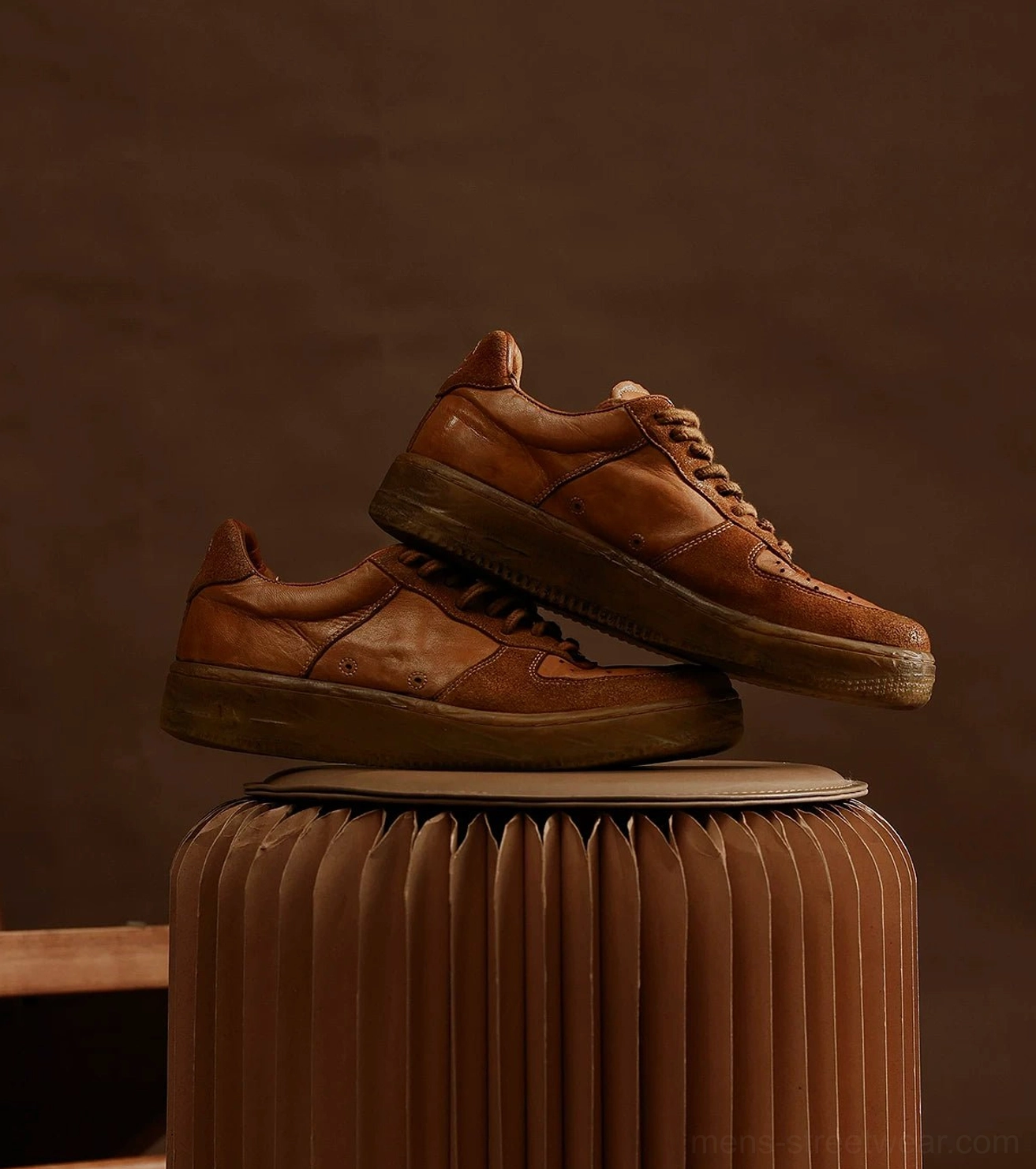 Brown distressed leather casual sneakers with tonal laces and vintage textured upper on dark studio background