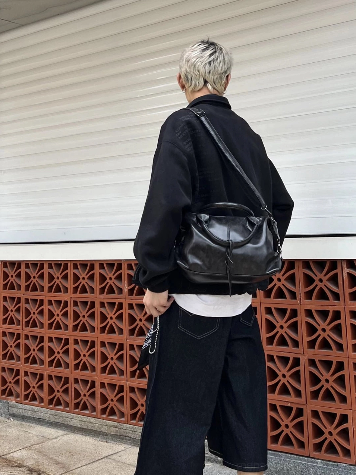 Black faux leather compact weekender bowling bag worn over the shoulder with black urban streetwear layers