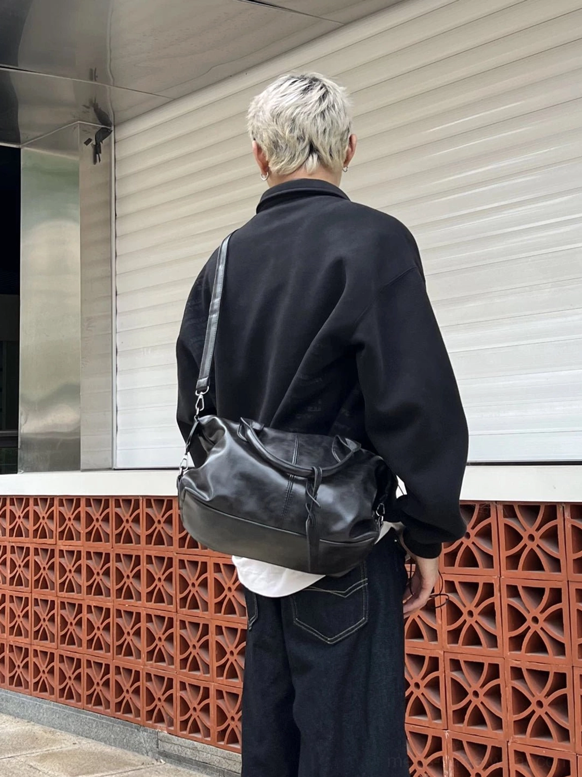 Side rear view of black vintage faux leather duffle bowling bag styled as a crossbody streetwear bag