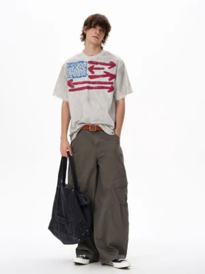 Male model wearing a vintage flag graphic oversized streetwear T-shirt with wide-leg gray cargo pants and black canvas tote bag