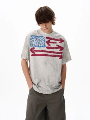Front close-up of a vintage flag graphic oversized T-shirt in acid-washed light gray heavyweight cotton with distressed retro chest print