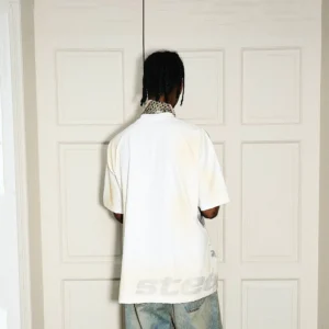 Back view of a faded cream oversized streetwear T-shirt with subtle gray lettering near the hem and vintage finish