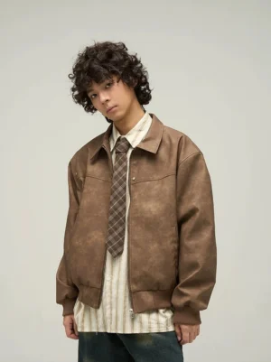 Male model wearing a vintage brown oversized faux leather bomber jacket with distressed texture, striped shirt, plaid tie, and dark jeans