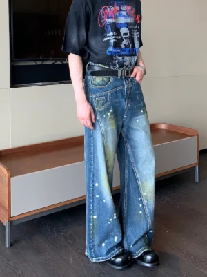 Left front three-quarter view of vintage blue paint splatter wide-leg jeans styled with a black graphic T-shirt, leather belt, and loafers