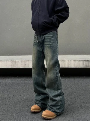 Front cropped view of vintage wash straight-leg streetwear jeans with faded denim, thigh whiskering, long stacked hem, and chain-style waist detail