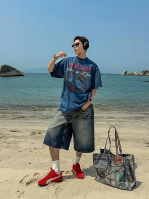 Vintage washed blue wide-leg denim culotte shorts worn with graphic t-shirt and red sneakers at the beach
