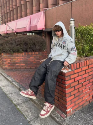 Male streetwear model wearing vintage denim platform sneakers with an army graphic hoodie and baggy black jeans in an urban street setting