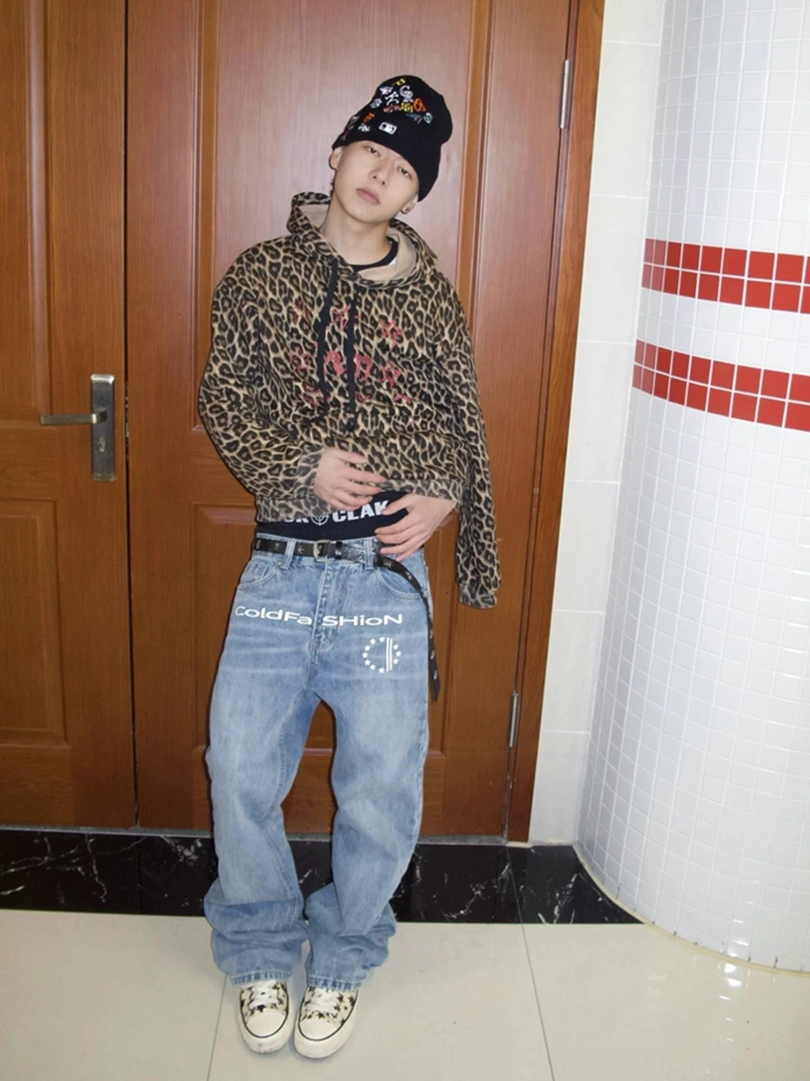 Male model wearing light blue vintage washed flare jeans with front graphic and elongated Seoul streetwear silhouette in an indoor corridor