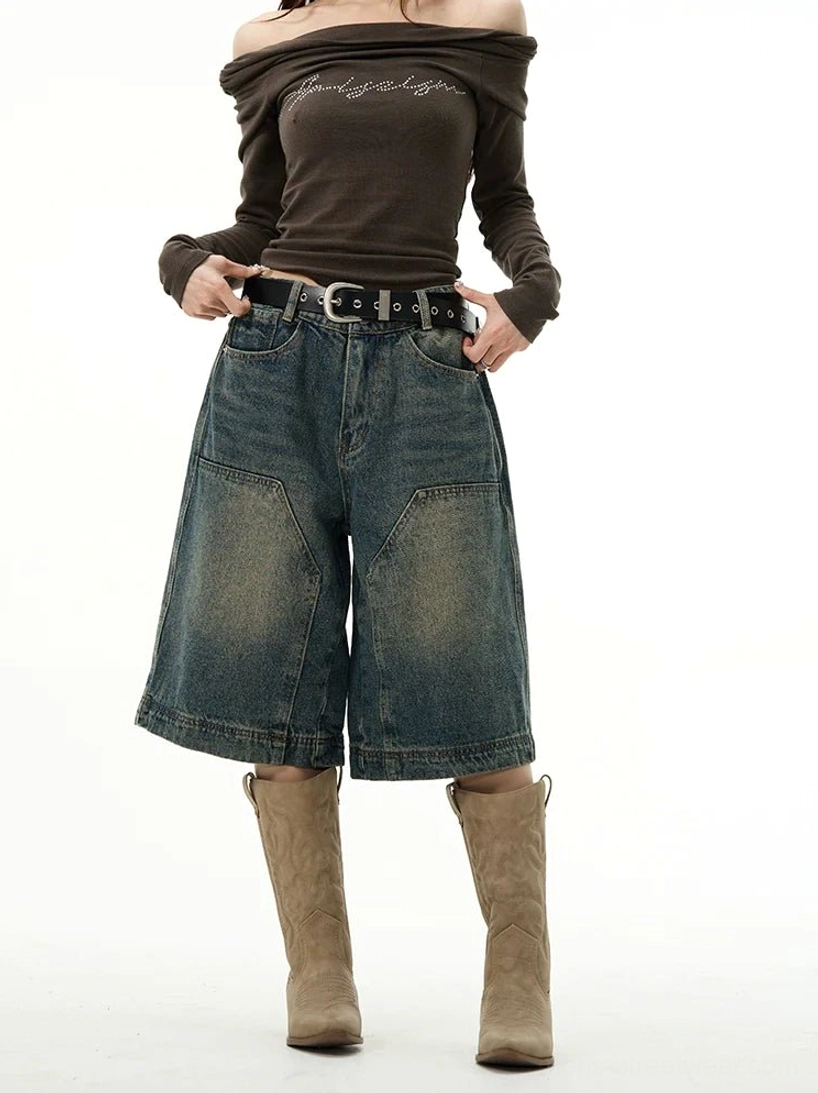 Blue wide-leg denim shorts in a relaxed baggy fit styled with an off-shoulder brown top, leather belt, and western knee-high boots