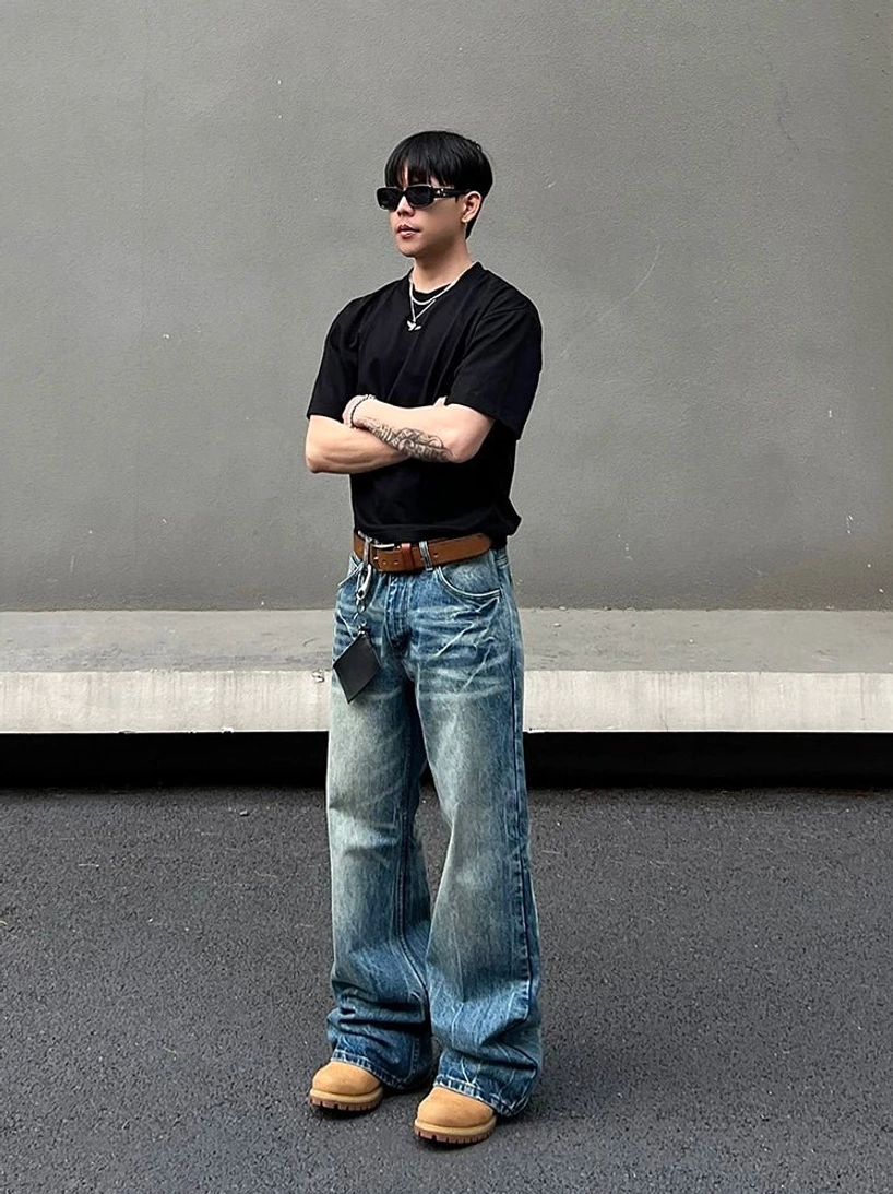 Front view of relaxed faded blue wide leg streetwear jeans styled with black top sunglasses and leather belt