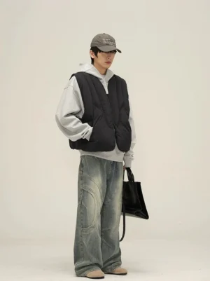 Three-quarter view of faded blue wide-leg streetwear jeans styled with a gray hoodie black puffer vest and baseball cap
