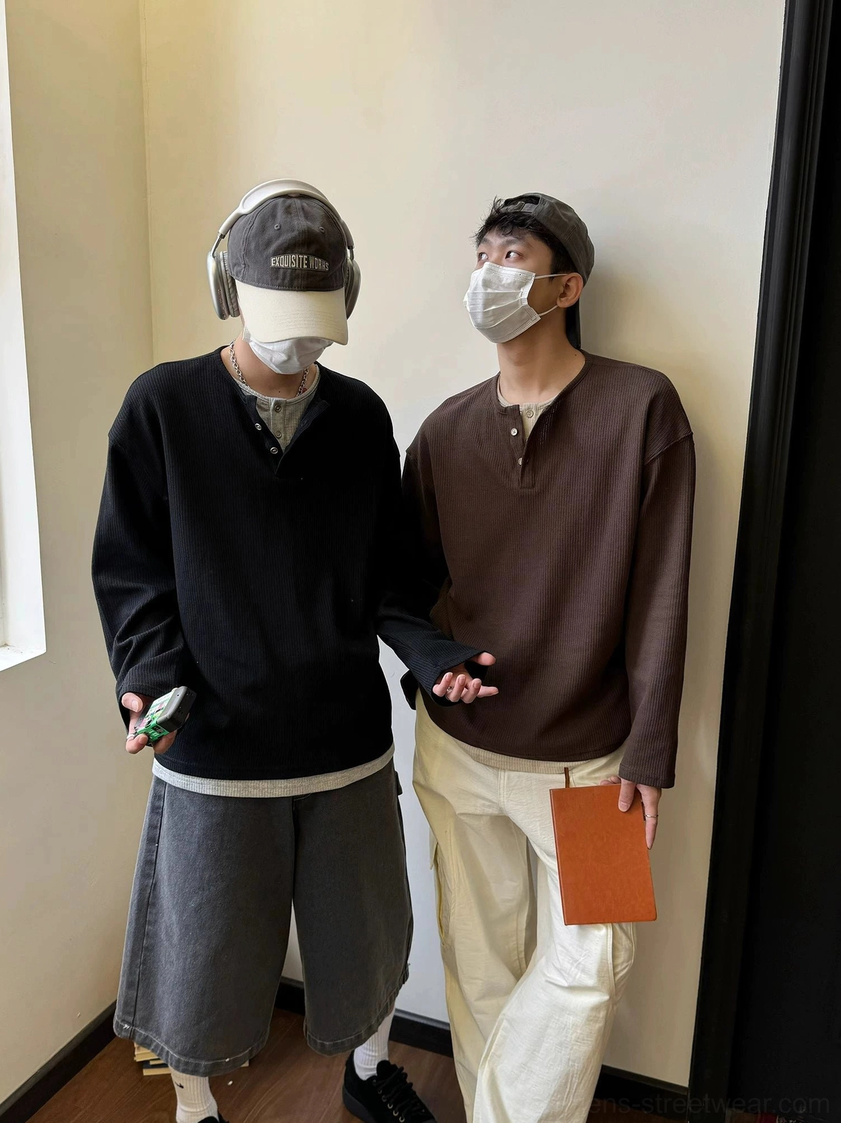 Two male models wearing relaxed black and dark brown waffle knit Henley shirts with wide-leg bottoms in a vintage streetwear studio