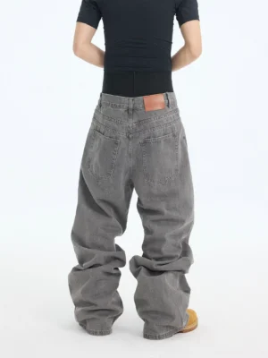 Back view of washed ash baggy denim jeans showing rear pockets, waist patch, faded cotton texture, and stacked loose hems