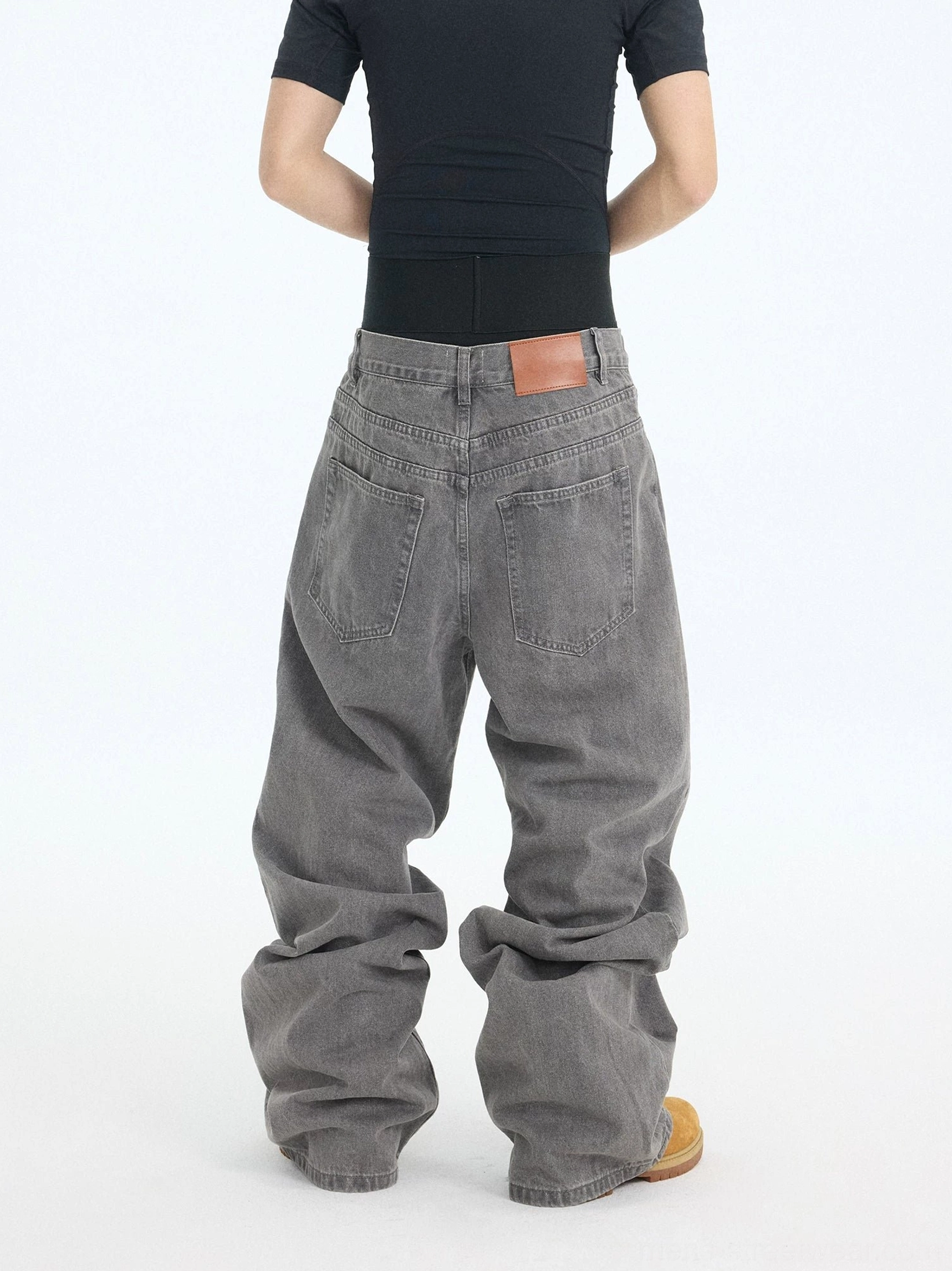 Back view of washed ash baggy denim jeans showing rear pockets, waist patch, faded cotton texture, and stacked loose hems