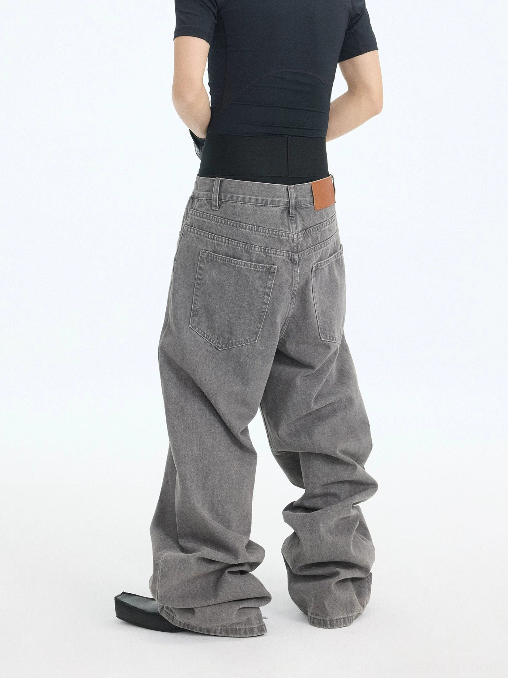 Rear side view of wide-leg washed ash streetwear jeans with leather waist patch and heavily stacked wrinkled hem