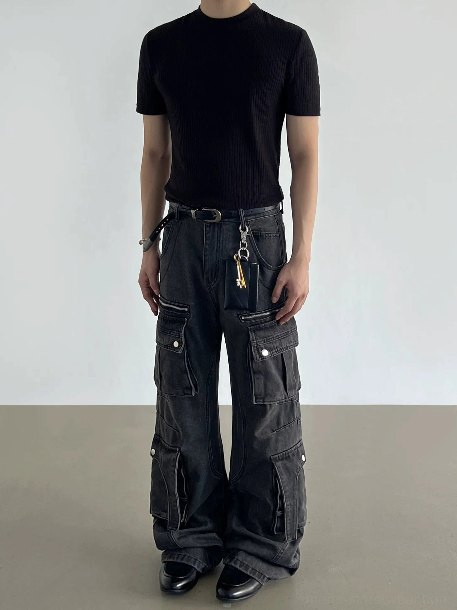 Full model view of washed black cargo jeans with oversized flap pockets, relaxed wide-leg fit, and hanging waist accessory