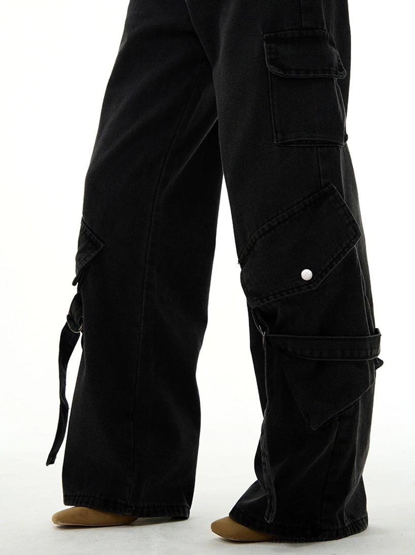 Close-up side view of washed black cargo denim jeans showing snap-button pocket straps and wide-leg hem