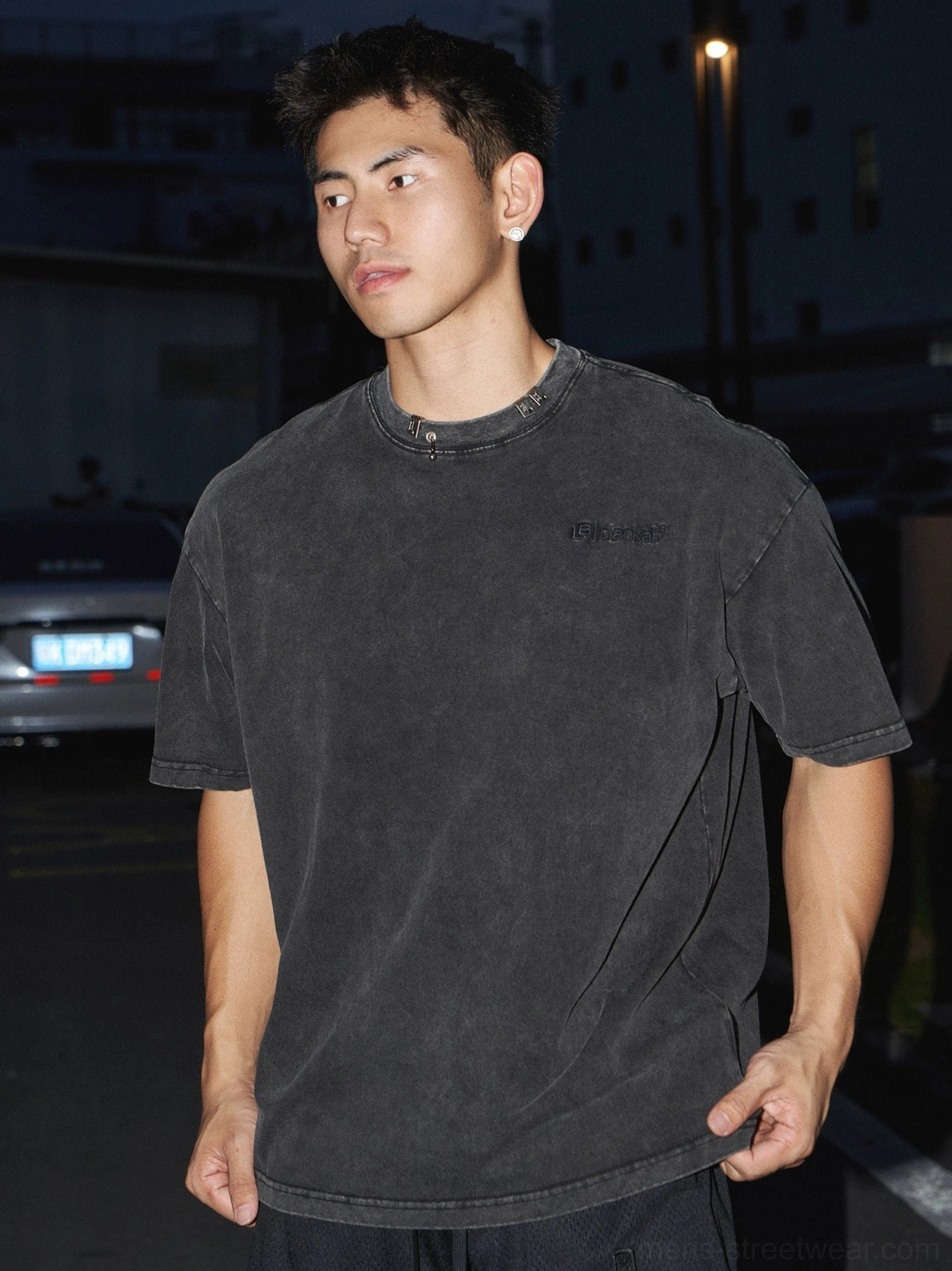 Close-up of washed black cotton oversized T-shirt showing vintage faded texture, refined crew neck trim, and subtle chest embroidery