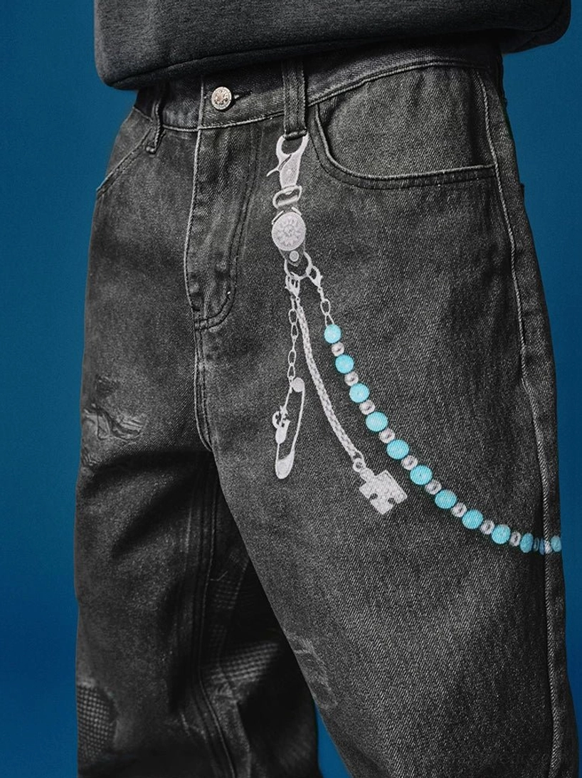 Close-up of washed black distressed wide-leg jeans showing the button fly, vintage denim texture, and beaded decorative waist chain