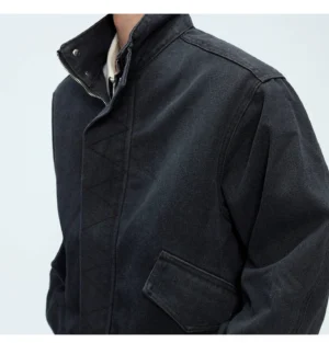 Washed black oversized cotton bomber jacket close-up showing stand snap collar zip closure flap pocket and reinforced shoulder seams