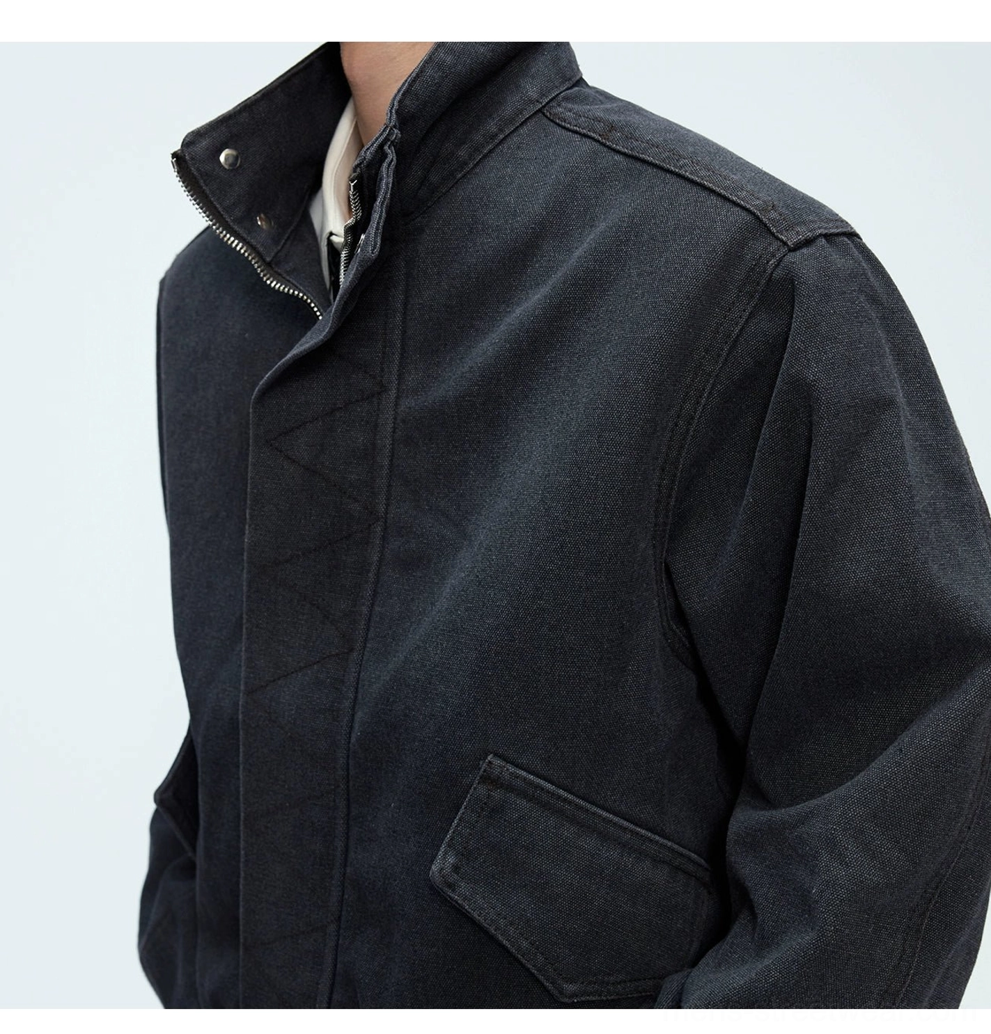Washed black oversized cotton bomber jacket close-up showing stand snap collar zip closure flap pocket and reinforced shoulder seams