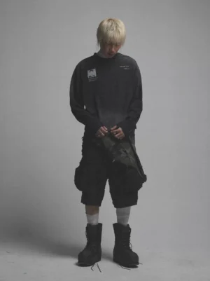 Front view of washed black prisoner-inspired graphic long sleeve tee styled with cargo shorts and boots in a modern streetwear outfit