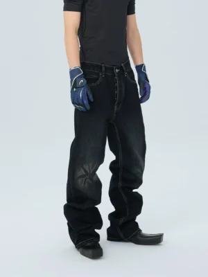 Front three quarter view of washed black stack fit streetwear jeans with faded knee whiskering, contrast stitching, wide relaxed legs, black T-shirt and leather boots