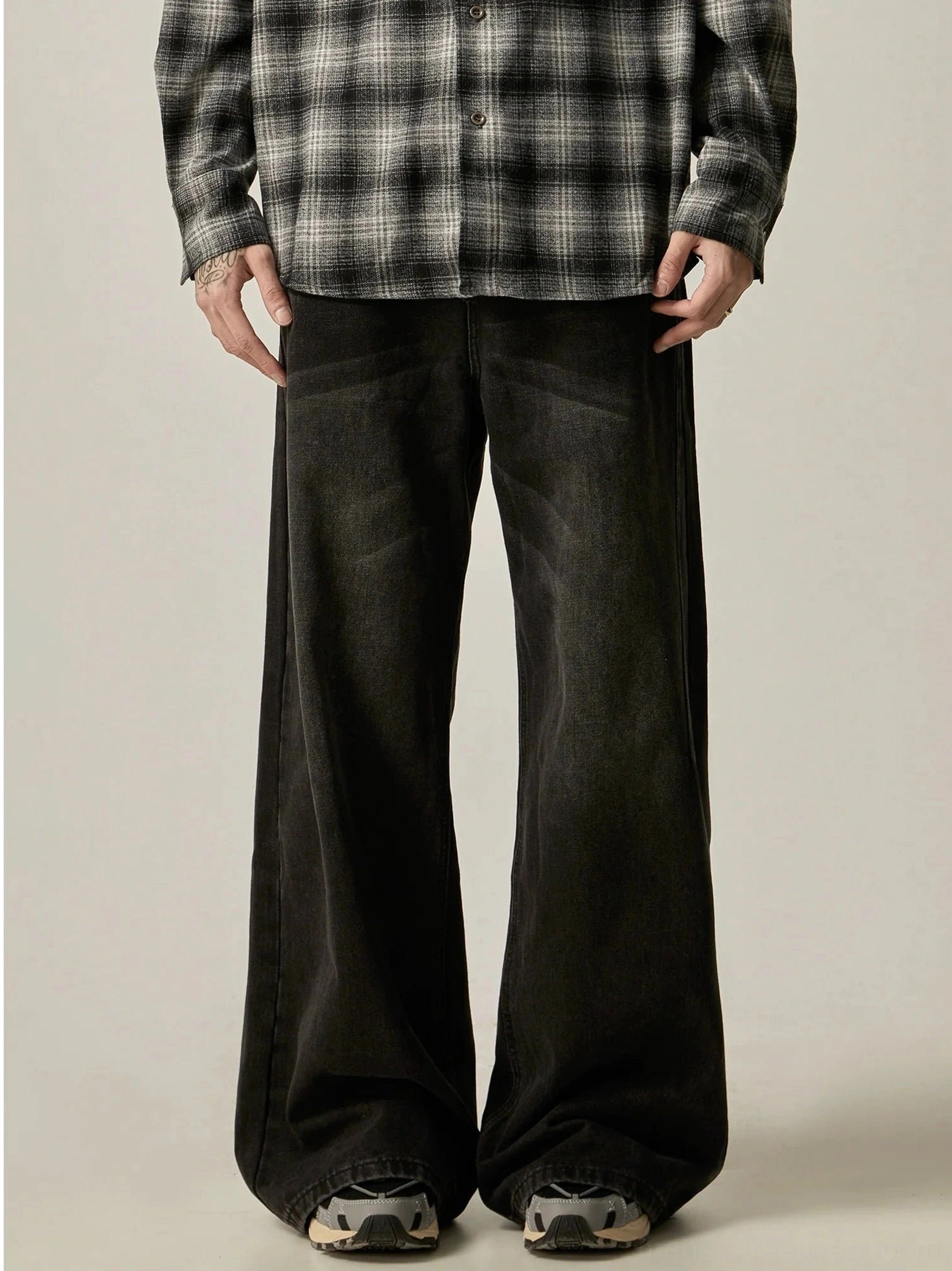 Front view of washed black ultra-wide leg jeans styled with a checkered shirt and retro running shoes in a neutral studio setting