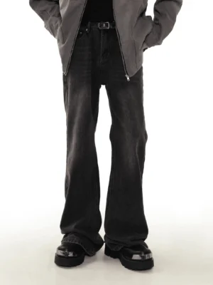 Male model wearing washed black flare jeans with a vintage faded denim finish, gray zip jacket, and platform boots in a white studio