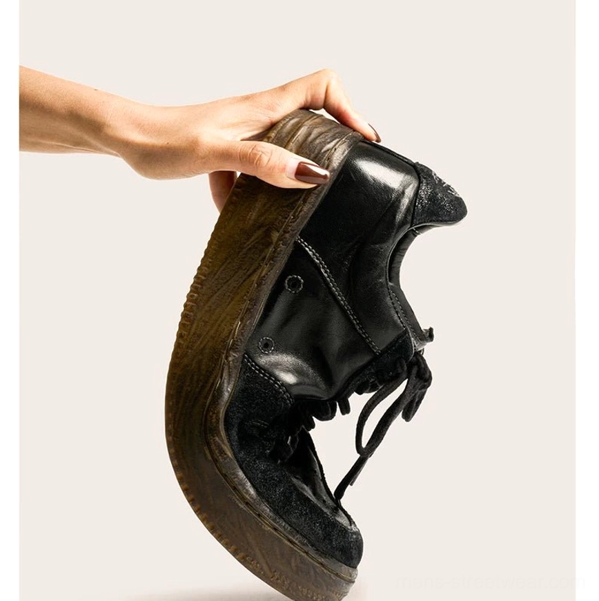 Hand holding washed black vintage leather court sneaker to demonstrate flexible soft horsehide leather upper and distressed brown rubber sole