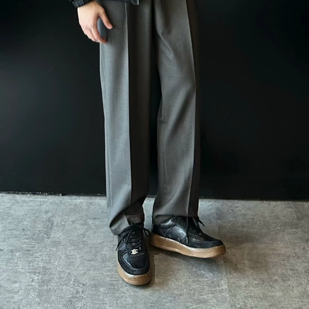 Front standing view of washed black vintage leather court sneakers paired with relaxed grey suit trousers in an urban minimalist outfit