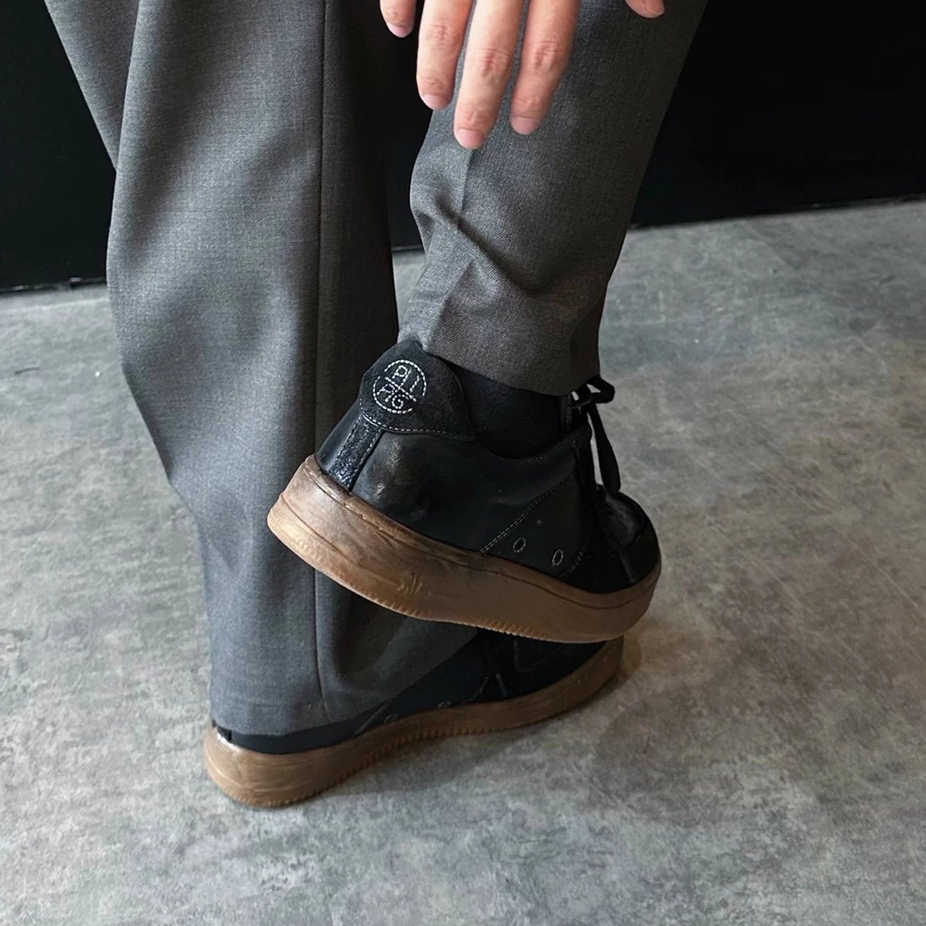 Low angle close-up of washed black vintage leather court sneaker heel and distressed gum outsole styled with tailored trousers