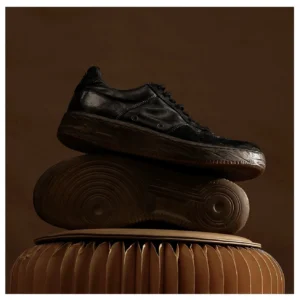 Washed black vintage leather court sneakers stacked on a warm brown display base showing aged leather texture and high-density gum rubber outsole tread