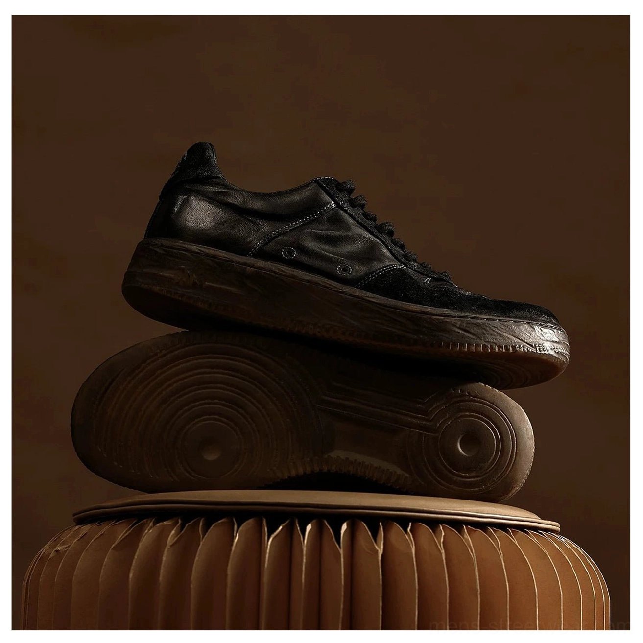 Washed black vintage leather court sneakers stacked on a warm brown display base showing aged leather texture and high-density gum rubber outsole tread
