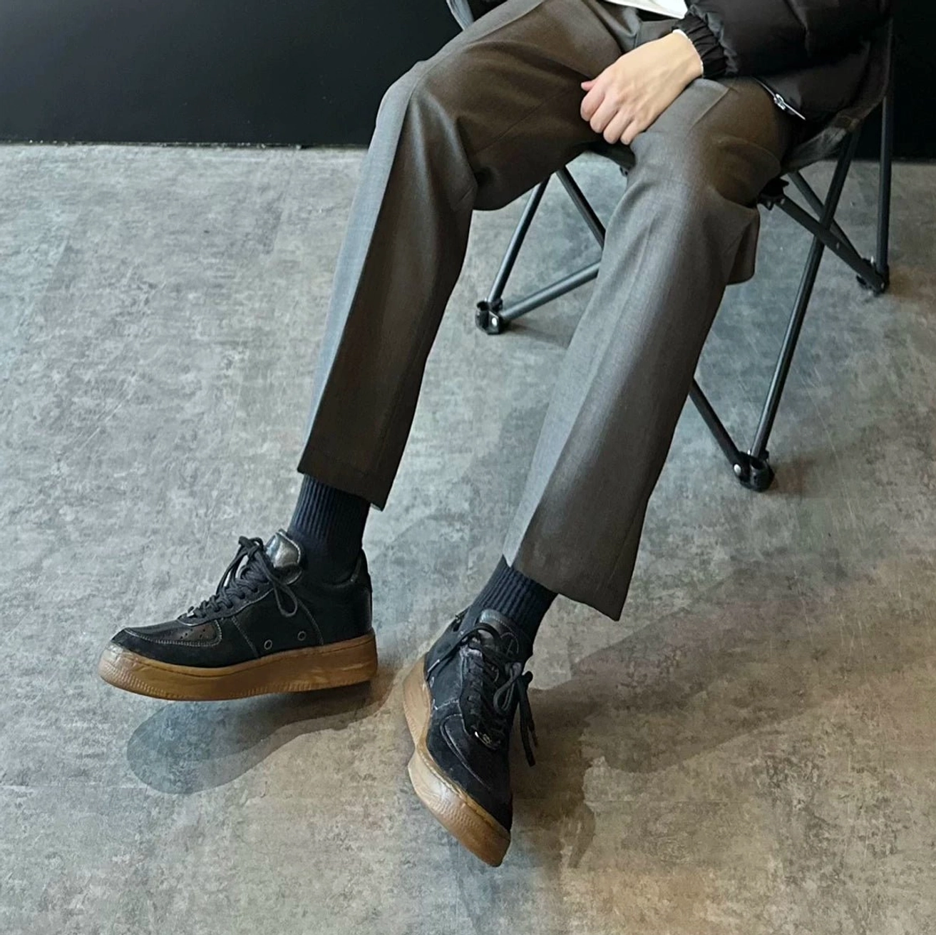Washed black vintage leather court sneakers styled with grey tailored suit trousers and black socks in a contemporary streetwear outfit