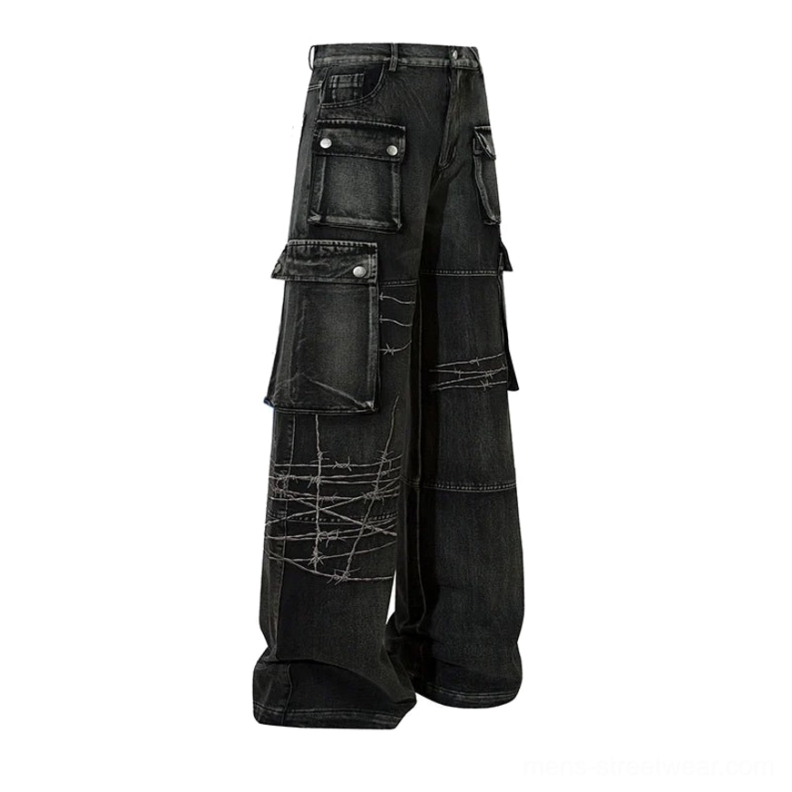 Flat lay side view of washed black wide-leg cargo denim jeans with metal snap cargo pockets, button fly, and contrast barbed wire embroidery