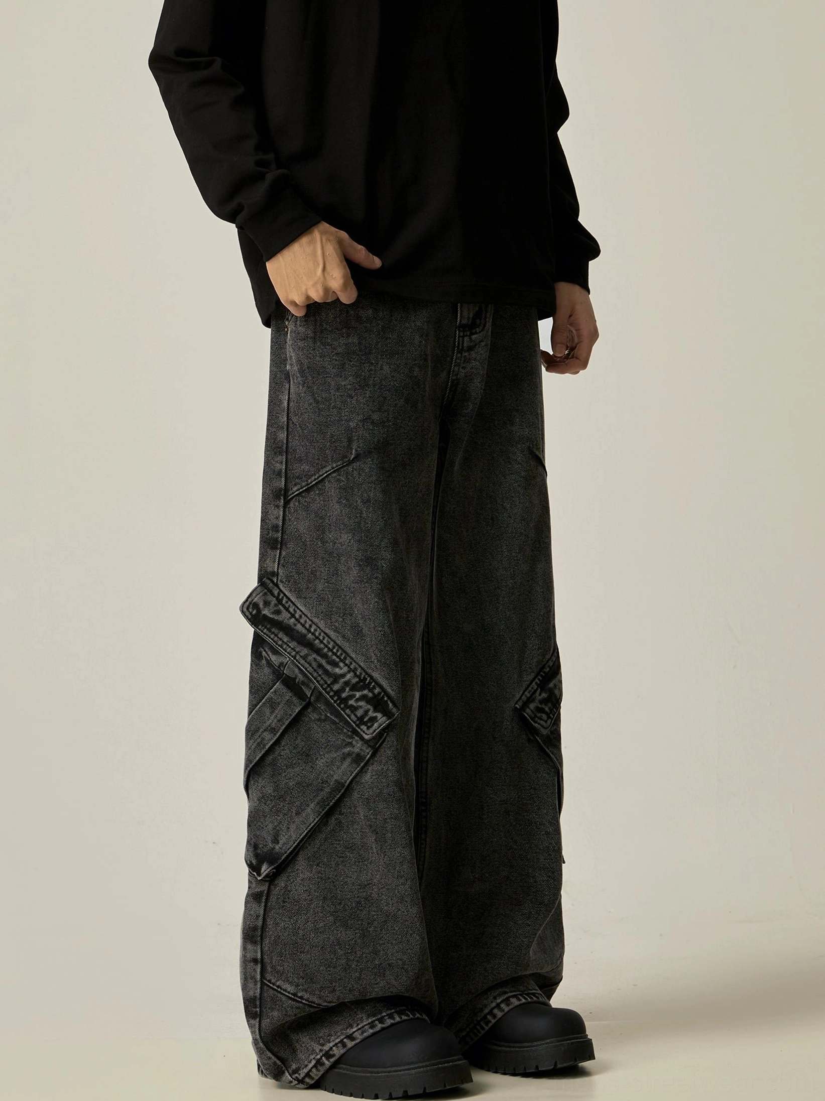Left three-quarter view of washed black wide-leg cargo jeans with large flap utility pockets styled with a black long-sleeve top and work boots