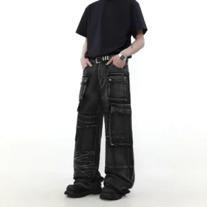 Side view of oversized washed black wide-leg cargo jeans featuring flap utility pockets, faded denim, and barbed wire embroidery